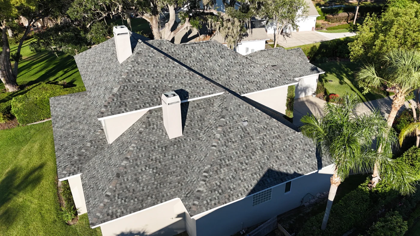 Greentek project photo — a drone view straight down onto a large Florida home with a new multi-tone grey architectural shingle roof and two white chimneys