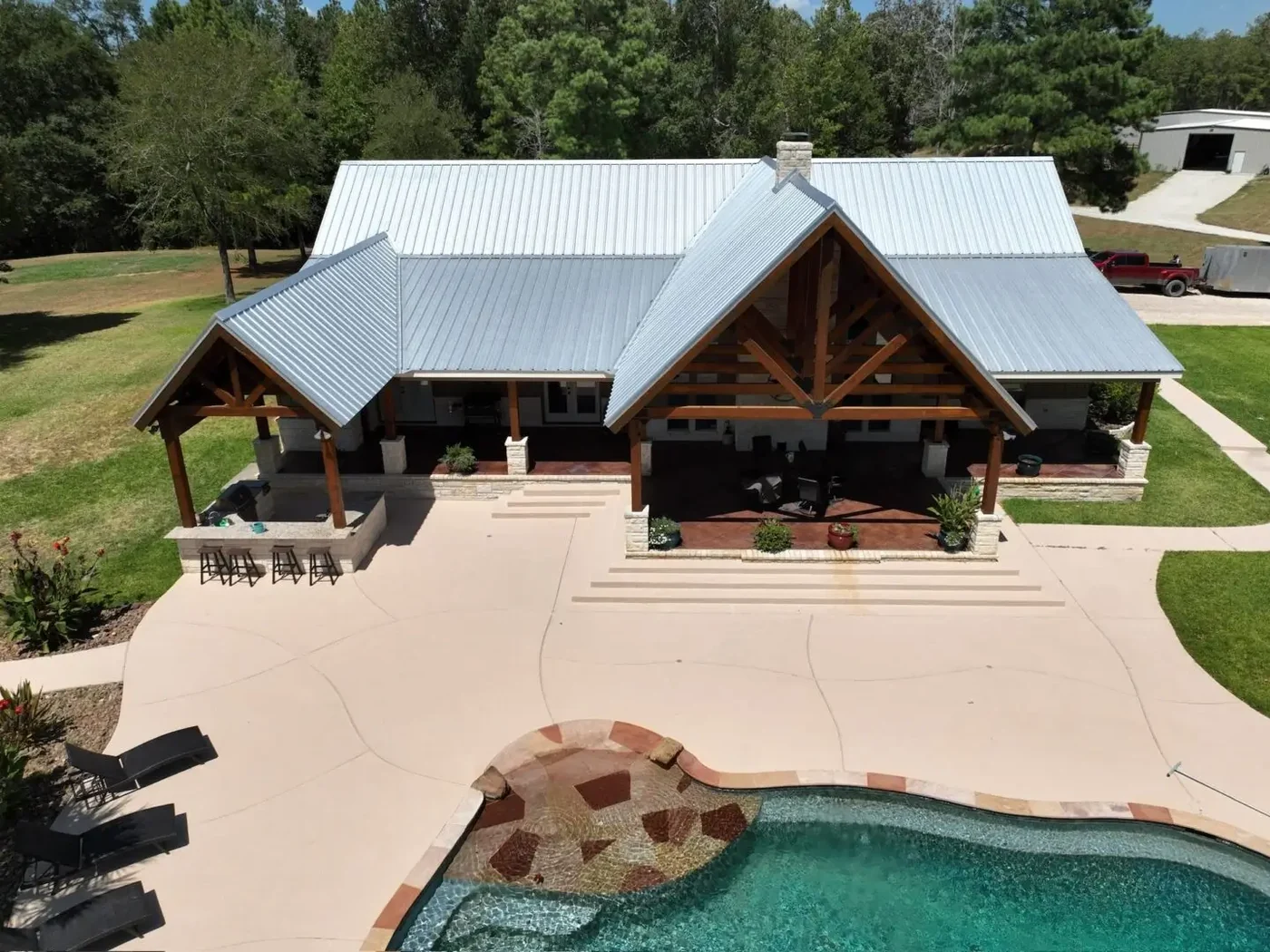 Roof Ryders project photo — a drone view of a timber-framed pool house under a new silver metal roof, looking down over the pool deck